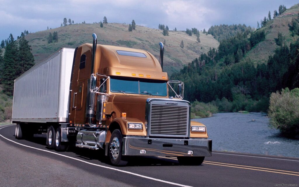 a brown semi truck driving down a road next to a river